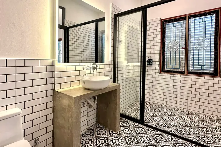 A bathroom with white subway tile, black-and-white patterned cement floor tiles, a concrete vanity, and a window of Chinese fretwork grilles with circular medallions painted red and blue.