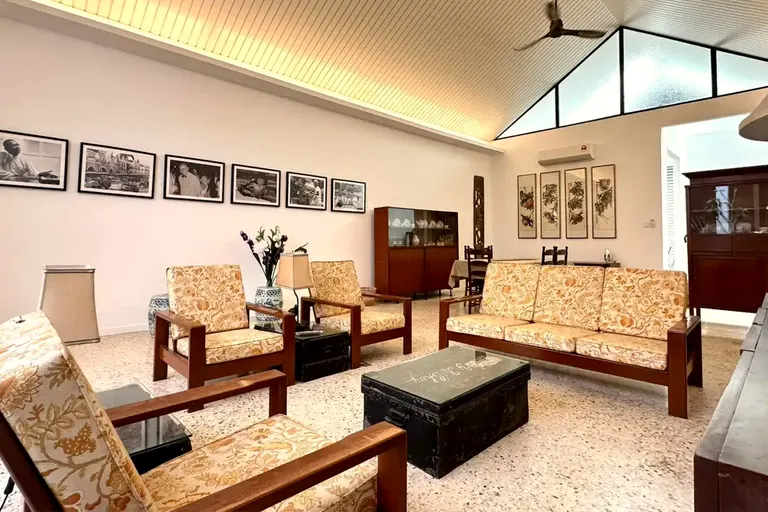 The living hall: terrazzo floor, vaulted timber ceiling with black-framed clerestory, a wall of framed photographs, a teak lounge suite with marigold floral cushions.